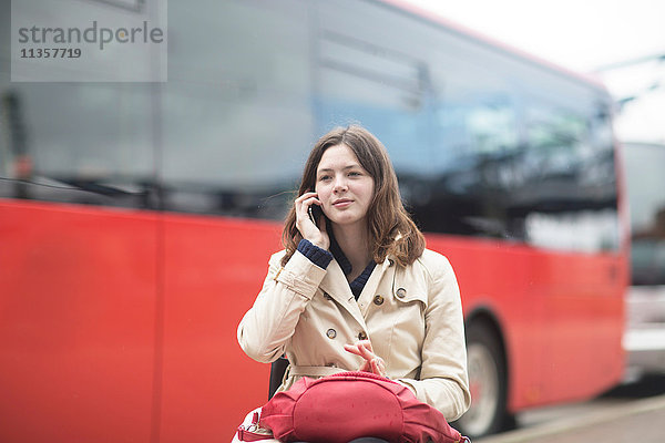 Junge Frau  die am Busbahnhof im Rollstuhl mit einem Smartphone telefoniert