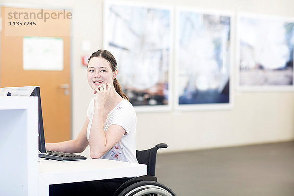 Junge Studentin im Rollstuhl mit Computer am Schreibtisch