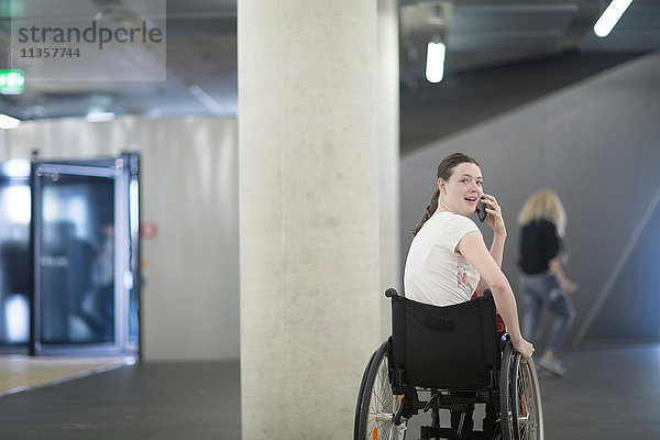 Junge Frau im Rollstuhl in Tiefgarage mit Smartphone