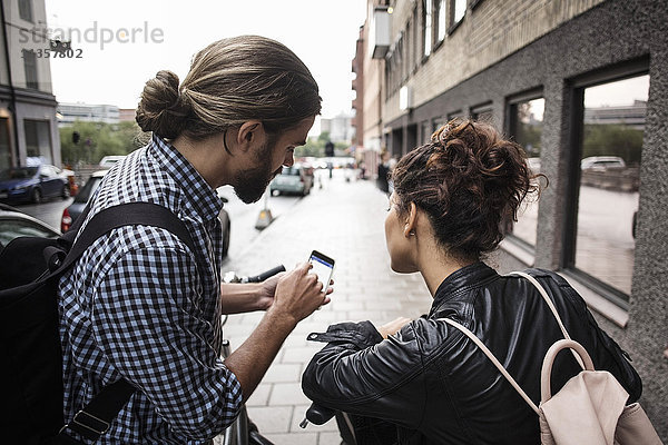 Mann zeigt Smartphone einem Freund auf dem Bürgersteig in der Stadt