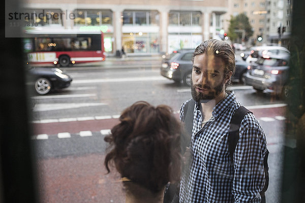 Mann im Gespräch mit Freund gegen Stadtstraße durch Glasfenster gesehen