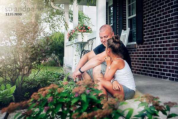 Seitenansicht von Vater und Tochter beim Plaudern auf der Veranda sitzend