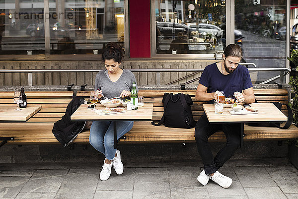 Volle Länge des Mannes und der Frau  die Nahrung am Bürgersteigcafe haben