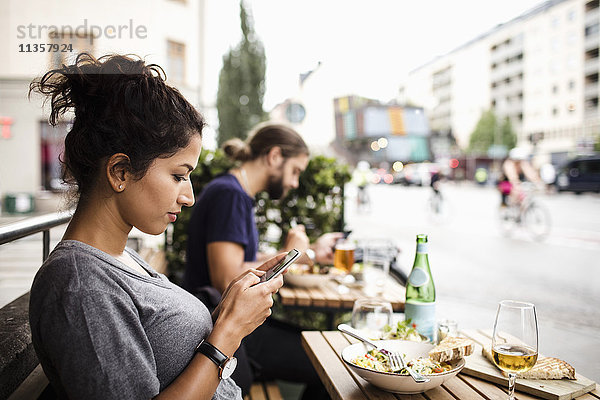 Seitenansicht der Frau SMS während des Essens im Straßencafé in der Stadt