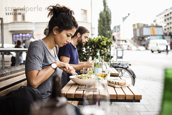 Seitenansicht von Mann und Frau beim Mittagessen im Straßencafé in der Stadt
