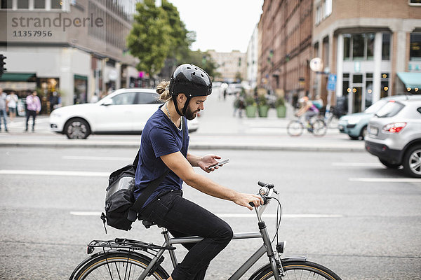 Seitenansicht des Mannes mit dem Handy beim Radfahren auf der Stadtstraße