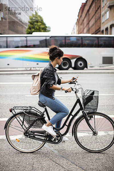 Seitenansicht der Frau mit dem Handy beim Radfahren auf der Stadtstraße