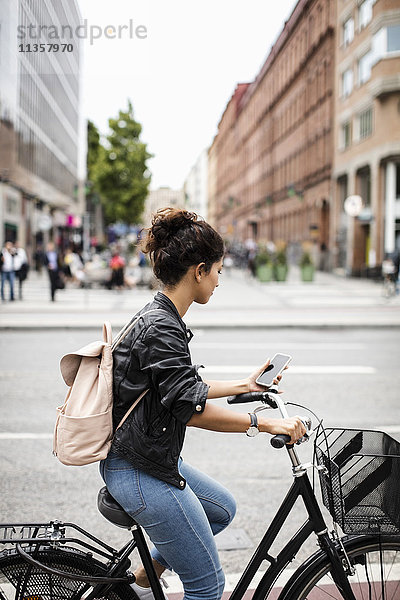 Frau schaut auf das Telefon  während sie auf der Stadtstraße Fahrrad fährt.