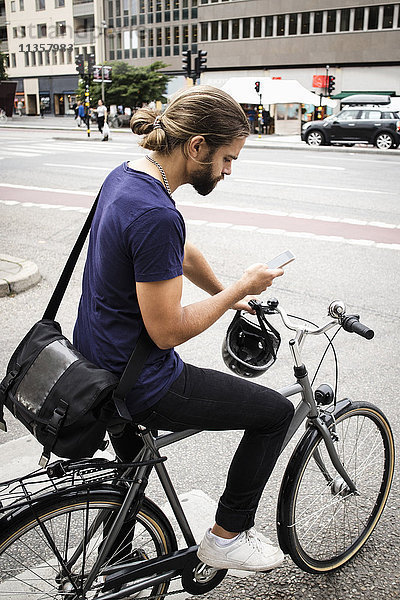 Mann mit Fahrrad mit Handy im Stehen auf der Stadtstraße