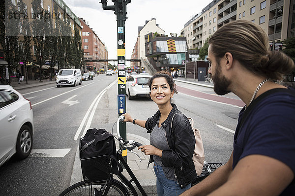Lächelnde Frau mit Fahrrad  die einen Freund ansieht  während sie mitten in der Stadt steht.