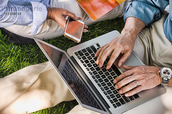 Geschäftsmann und -frau sitzen im Freien auf Rasen  mit Laptop  Mittelteil