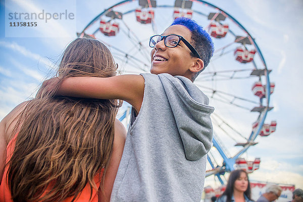 Rückansicht eines Teenager-Paares  das vor dem Riesenrad im Vergnügungspark über die Schulter schaut