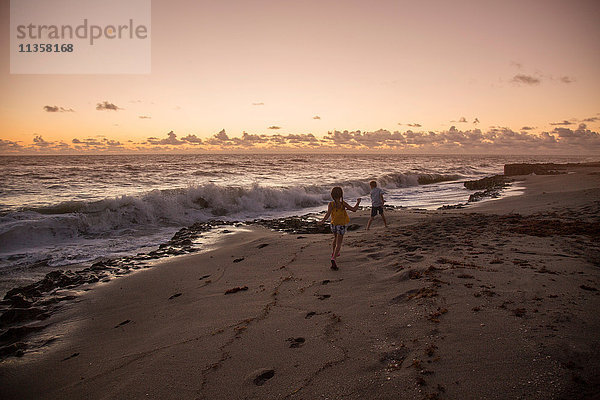 Junge und Schwester laufen bei Sonnenaufgang am Strand  Blowing Rocks Preserve  Jupiter Island  Florida  USA