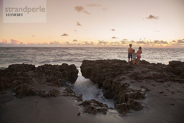 Junge und Schwestern schauen bei Sonnenaufgang von den Felsen hinaus  Blowing Rocks Preserve  Jupiter Island  Florida  USA