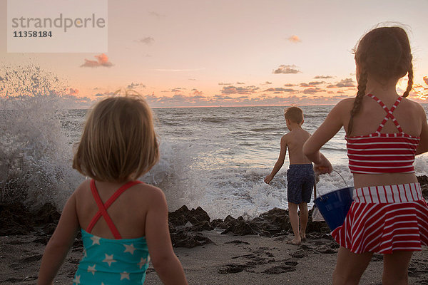 Junge und Schwestern beobachten plätschernde Wellen bei Sonnenaufgang  Blowing Rocks Preserve  Jupiter Island  Florida  USA