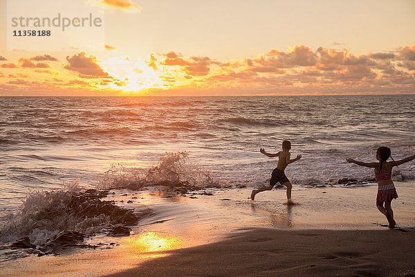 Mädchen und Bruder laufen bei Sonnenaufgang am Strand  Blowing Rocks Preserve  Jupiter Island  Florida  USA