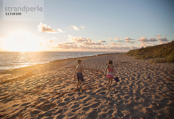 Junge und Schwester spazieren bei Sonnenaufgang am Strand entlang  Blowing Rocks Preserve  Jupiter Island  Florida  USA