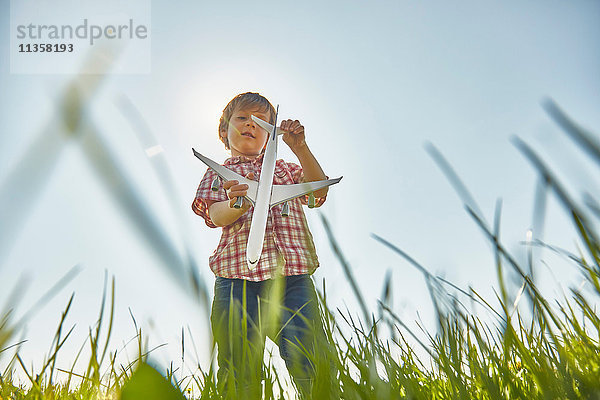 Niedrigwinkel-Ansicht eines Jungen  der im Gras steht und das Heck eines Spielzeugflugzeugs kontrolliert