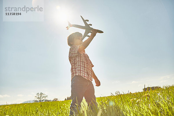 Junge auf sonnenbeschienenem Feld mit blauem Himmel spielt mit Spielzeugflugzeug