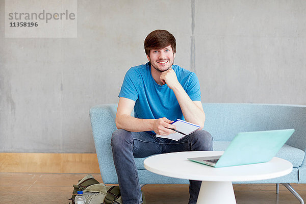 Porträt eines jungen männlichen Studenten  der auf einem Studienplatz-Sofa an einer Hochschule sitzt