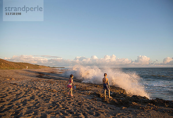 Junge und Schwester beobachten plätschernde Wellen vom Strand aus  Blowing Rocks Preserve  Jupiter Island  Florida  USA