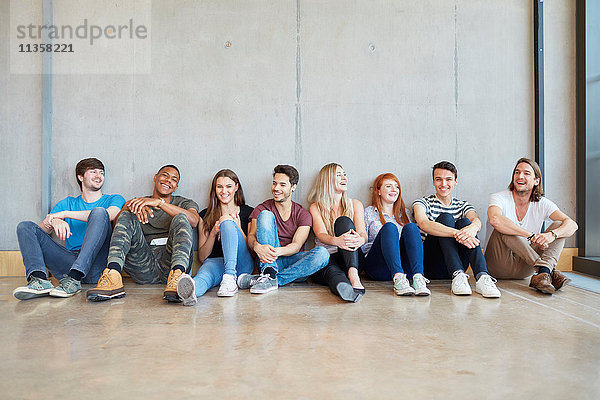 Gruppenbild von männlichen und weiblichen Studenten  die in einer Reihe auf dem Boden einer Hochschule sitzen