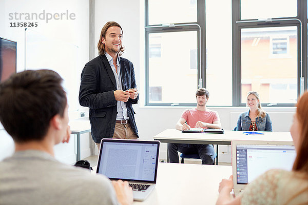 Männlicher Dozent  der Studenten mit Laptops im Klassenzimmer von Hochschulen unterrichtet