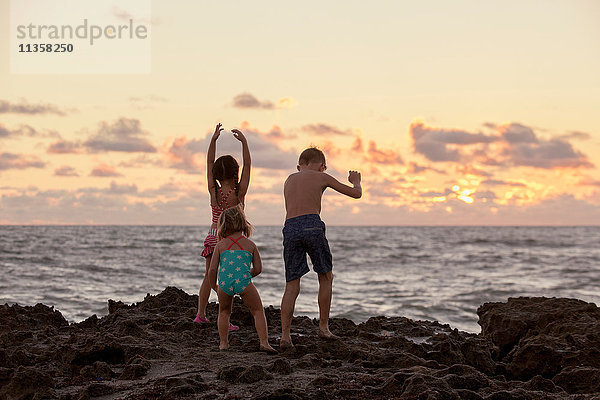 Rückansicht eines Jungen und seiner Schwestern  die bei Sonnenaufgang am Strand spielen  Blowing Rocks Preserve  Jupiter Island  Florida  USA