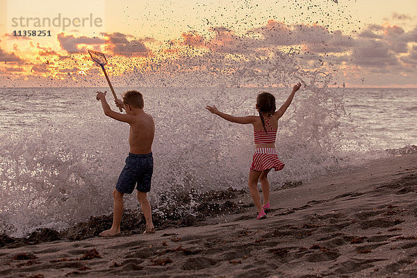 Rückansicht eines Jungen und einer Schwester  die bei Sonnenaufgang in plätschernden Wellen spielen  Blowing Rocks Preserve  Jupiter Island  Florida  USA