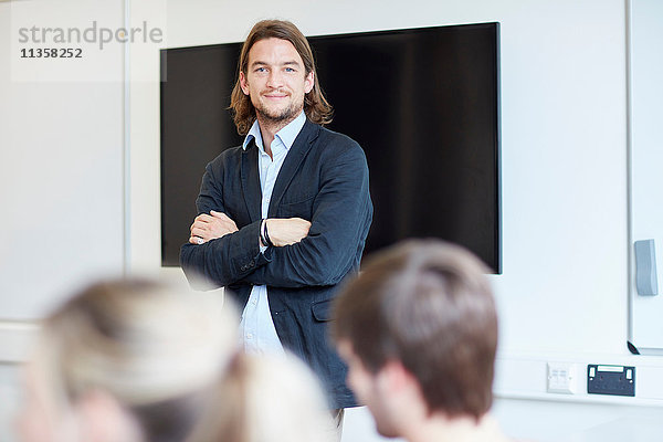 Porträt eines männlichen Dozenten mit verschränkten Armen im Klassenzimmer einer Hochschule