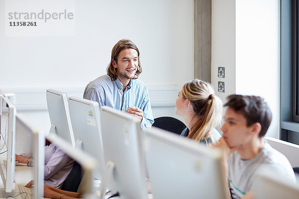 Männlicher Dozent im Gespräch mit Student im Computerraum der Hochschule