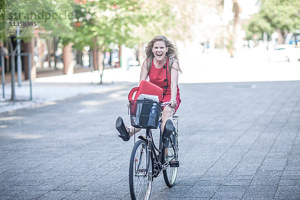 Glückliche Geschäftsfrau freilaufend auf dem Fahrrad in der Stadt