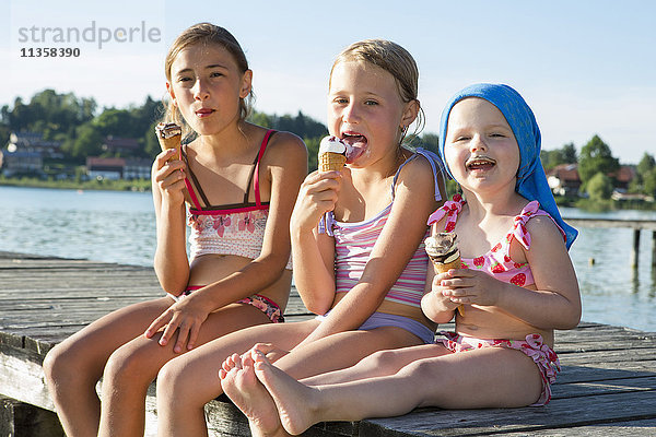 Zwei Schwestern und ein weibliches Kleinkind am Pier beim Essen von Eiswaffeln  Seeoner See  Bayern  Deutschland
