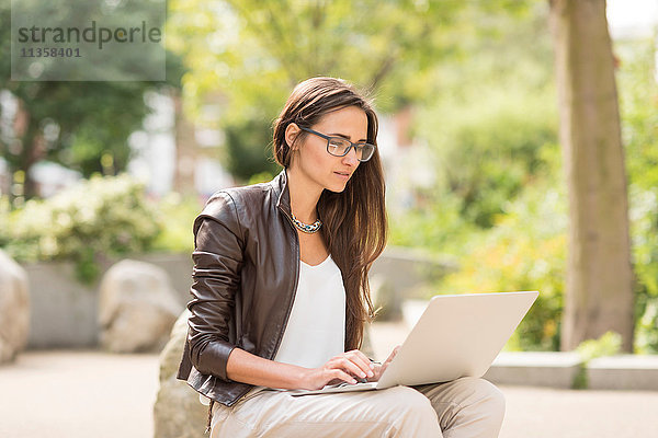 Junge Geschäftsfrau beim Tippen am Laptop im Stadtpark