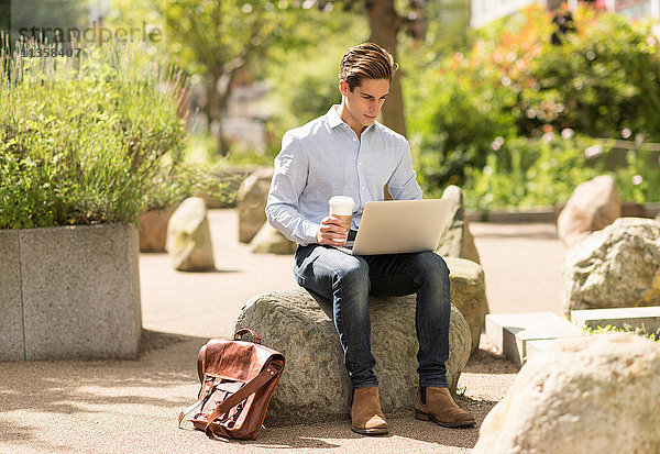 Junger Geschäftsmann liest Laptop im Stadtpark