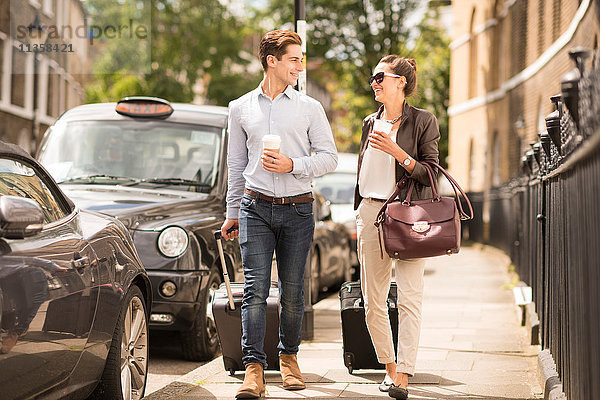 Ein junger Geschäftsmann und eine junge Frau  die mit einem Radkoffer auf der City Street  London  UK  spazieren gehen.