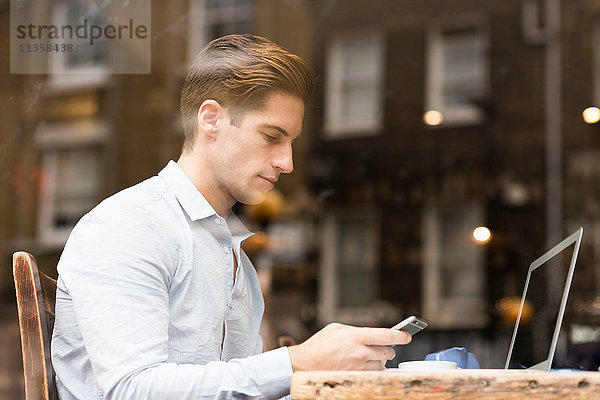 Fensteransicht eines jungen Geschäftsmannes beim Lesen von Smartphone-Texten im Cafe