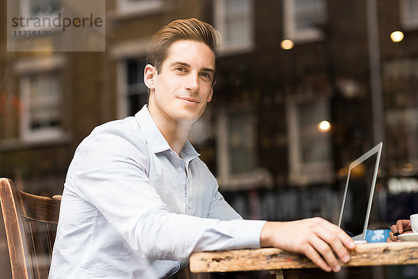Fensteransicht eines jungen Geschäftsmannes mit Laptop im Cafe