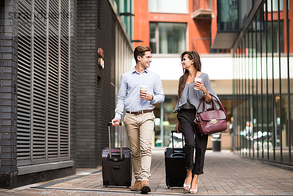 Junger Geschäftsmann und Frau mit fahrbaren Koffern beim Gehen und Sprechen  London  UK