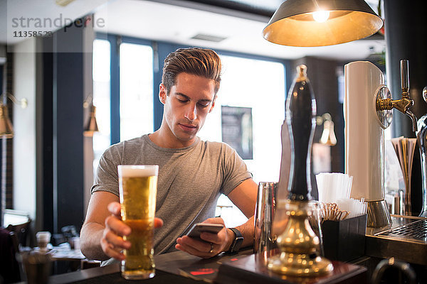 Junger Mann liest Smartphone in der Stadtbar