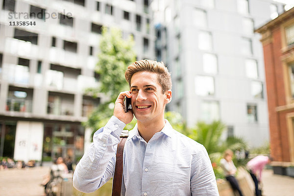 Junger Geschäftsmann im Gespräch auf dem Smartphone vor dem Stadtbüro  London  UK