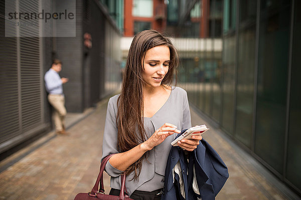 Junge Geschäftsfrau SMS auf Smartphone außerhalb des Büros  London  UK