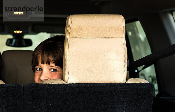 Porträt eines glücklichen Jungen  der vom Rücksitz des Autos aus über die Schulter schaut
