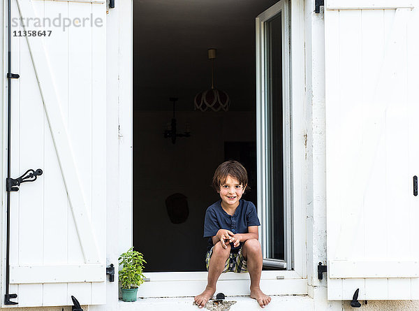 Porträt eines Jungen  der vor der Tür einer Ferienwohnung sitzt  Frankreich