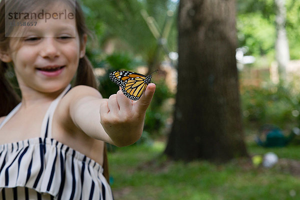 Mädchen hält Monarchfalter auf Finger lächelnd