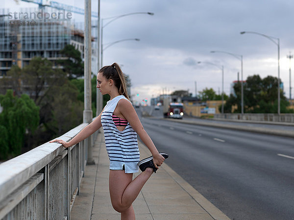 Junge Läuferin  die im Morgengrauen auf der Autobahnbrücke die Beine streckt