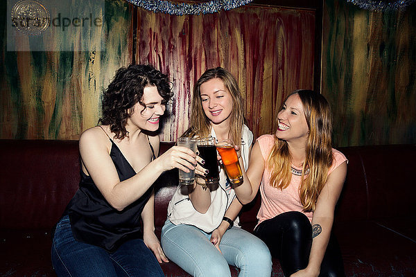 Drei erwachsene Freundinnen erheben ein Glas in einer Bar