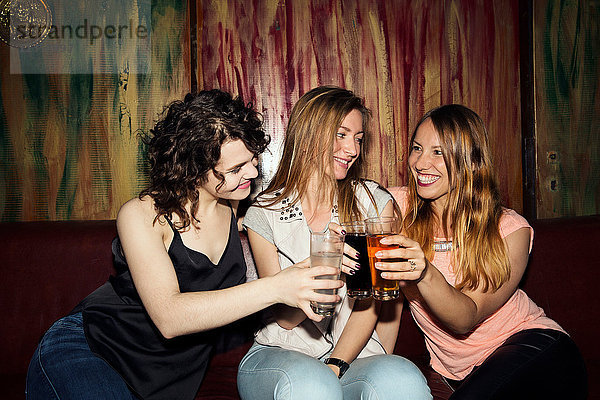 Drei erwachsene Freundinnen erheben ein Glas  während sie in einer Bar sitzen