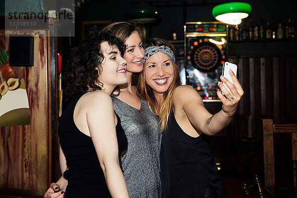 Drei erwachsene Freundinnen mit Smartphone-Selfie am Abend in einer Bar
