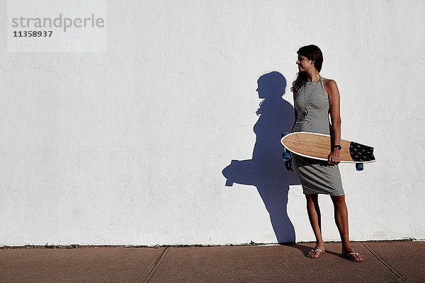 Coole junge Frau steht vor weißer Wand und hält Skateboard  New York  USA